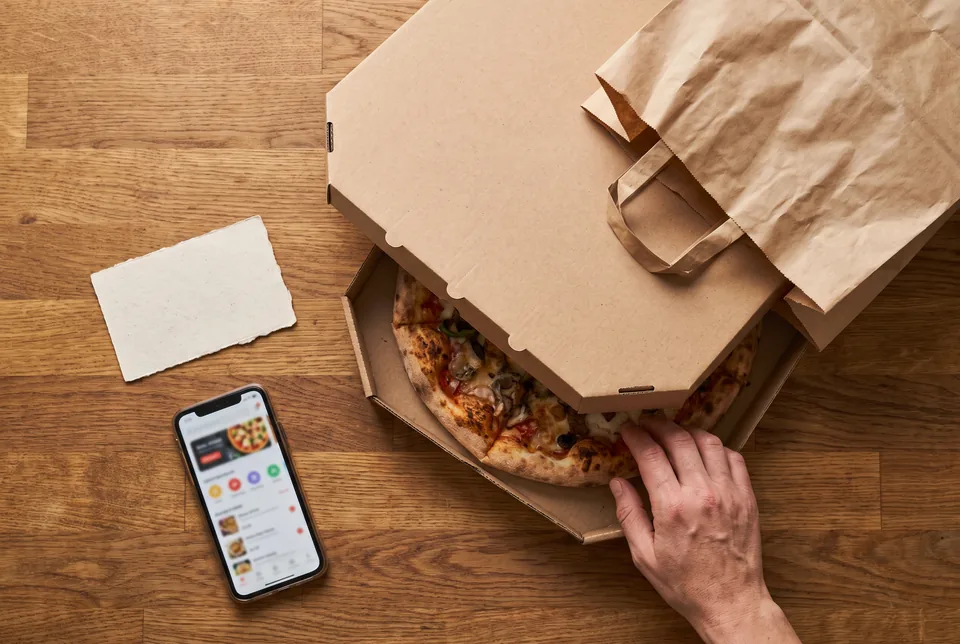Zamówienie pizzy na wynos w kartonie, obok telefon z ekranem zamówienia